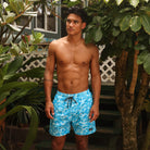 Man wearing blue swim shorts with a pattern standing outdoors among plants.