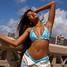 Woman in a blue and white bikini standing on a balcony with a cityscape background