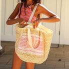 Woman holding a woven bag with a pink and white pattern, standing outdoors.
